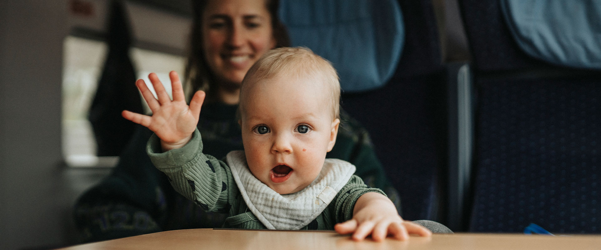 Baby waving, mother in the background
