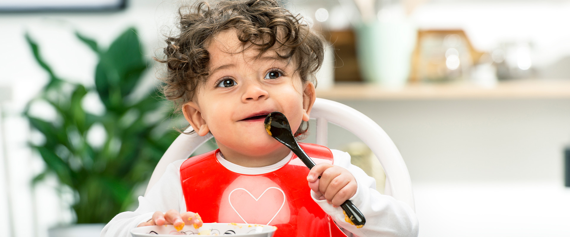 Baby with red bib eating with spoon